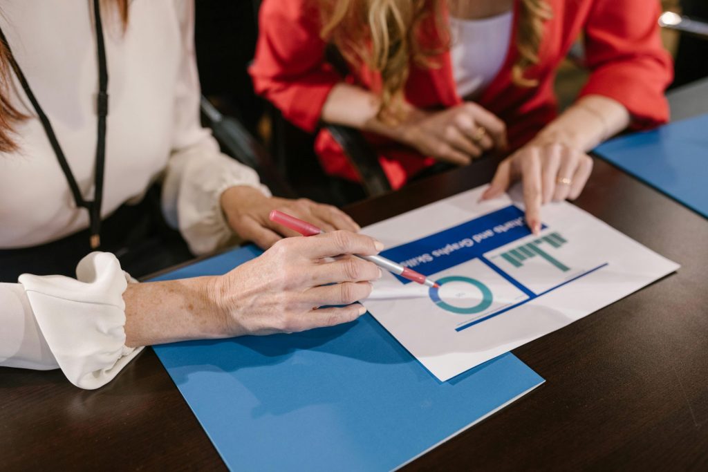 Deux femmes analysent des graphiques et des rapports d'entreprise lors d'une réunion autour d'une table en bois.