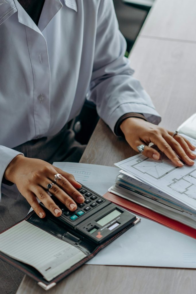 Le comptable effectue des calculs financiers à l'aide d'une calculatrice et consulte des documents sur un bureau.